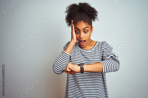 African american woman wearing navy striped t-shirt standing over isolated white background Looking at the watch time worried, afraid of getting late