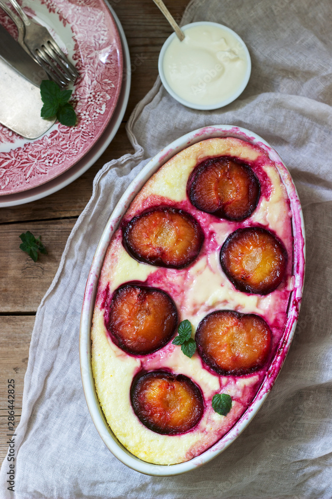 Tender curd casserole with plums and semolina, served with cinnamon and mint leaves on a wooden background.