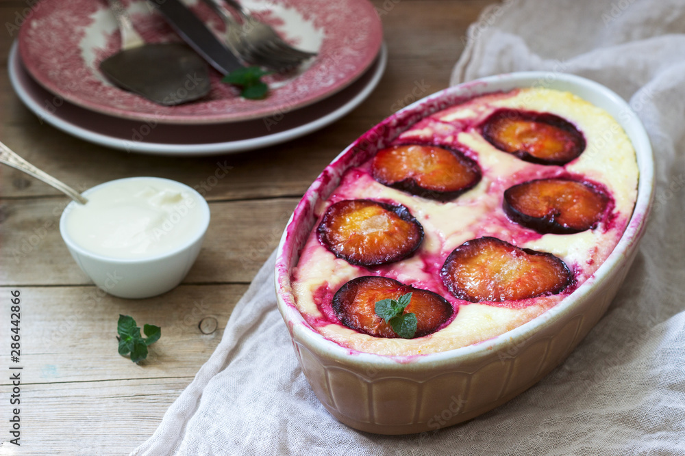Tender curd casserole with plums and semolina, served with cinnamon and mint leaves on a wooden background.