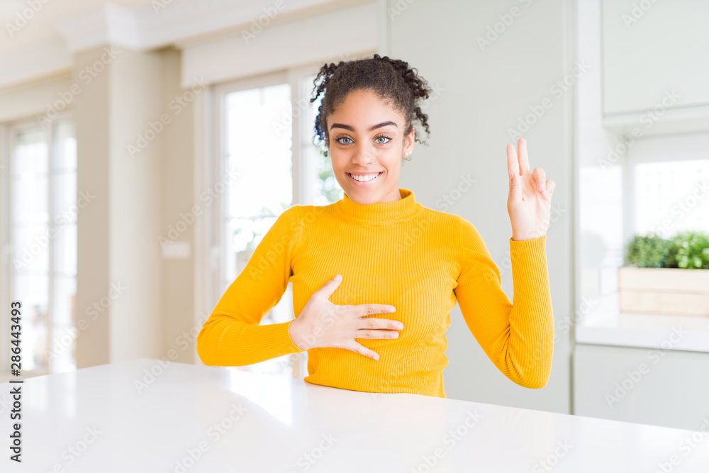 Beautiful african american woman with afro hair wearing a casual yellow sweater smiling swearing with hand on chest and fingers up, making a loyalty promise oath Beautiful african american woman with afro hair wearing a casual yellow sweater smiling swearing with hand on chest and fingers up, making a loyalty promise oath