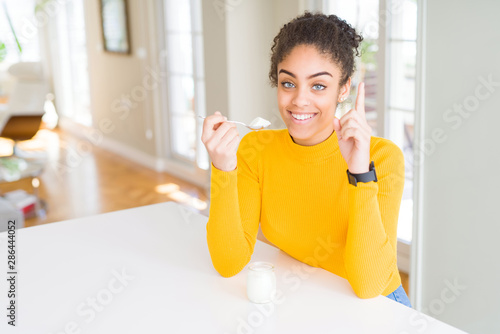 Young african american woman eating a healthy natural yogurt surprised with an idea or question pointing finger with happy face, number one