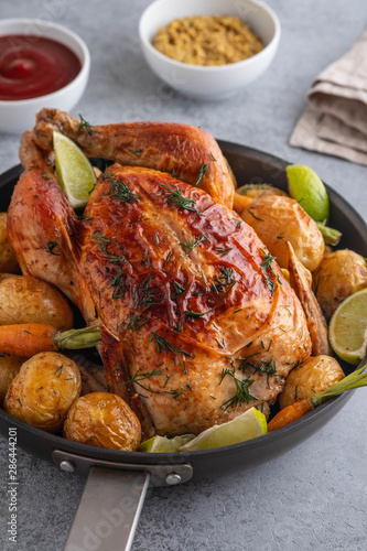 Roast chicken whole. Served on a plate with vegetables and baked potatoes. Front view.