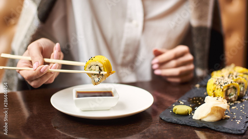 Woman relaxing and eating dinner in restaurant. Female client with manicure enjoying Japanese dish with soya sauce using food sticks. Oriental style lunch serving with wasabi and ginger.