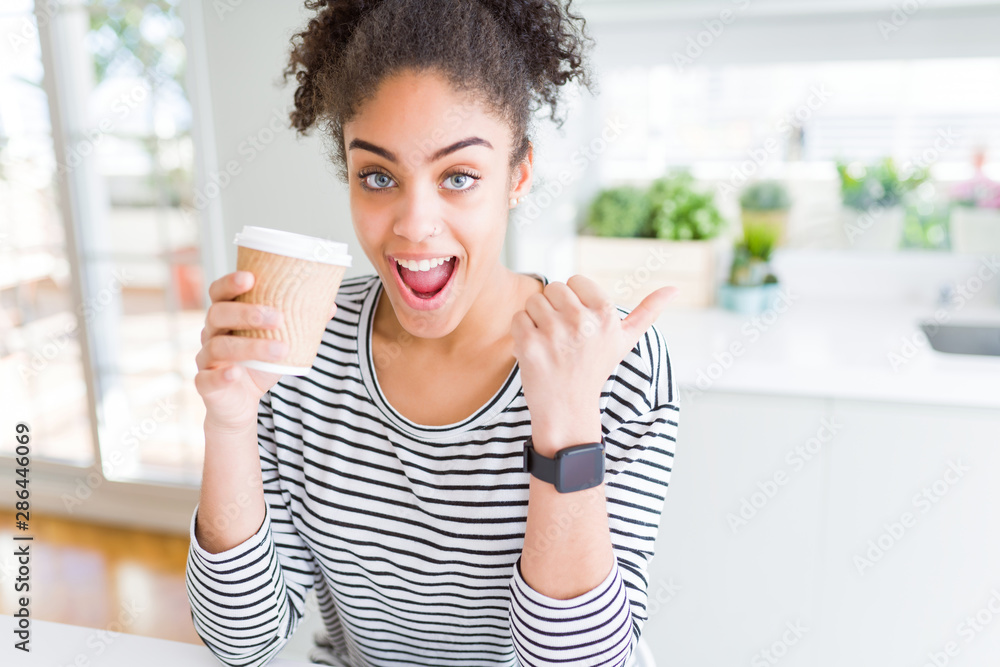 Young african american girl drinking a coffee on a take away paper cup pointing and showing with thumb up to the side with happy face smiling