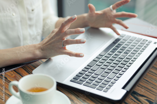 laptop on the table. female tense hands with outstretched fingers above the computer. white cup of tea next to a laptop. Stress, irritation.