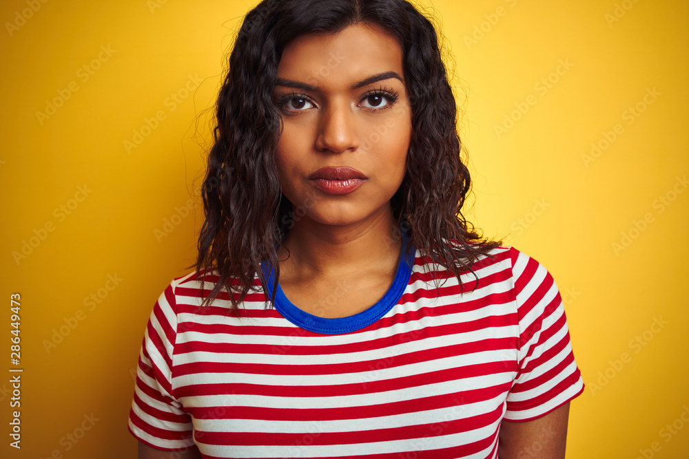Transsexual transgender woman wearing stiped t-shirt over isolated yellow background with a confident expression on smart face thinking serious Transsexual transgender woman wearing stiped t-shirt over isolated yellow background with a confident expression on smart face thinking serious