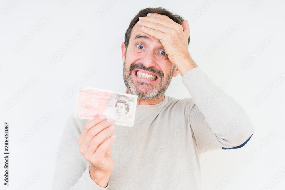 Senior man holding fifty pounds bank note over isolated background stressed with hand on head, shocked with shame and surprise face, angry and frustrated. Fear and upset for mistake. Senior man holding fifty pounds bank note over isolated background stressed with hand on head, shocked with shame and surprise face, angry and frustrated. Fear and upset for mistake.