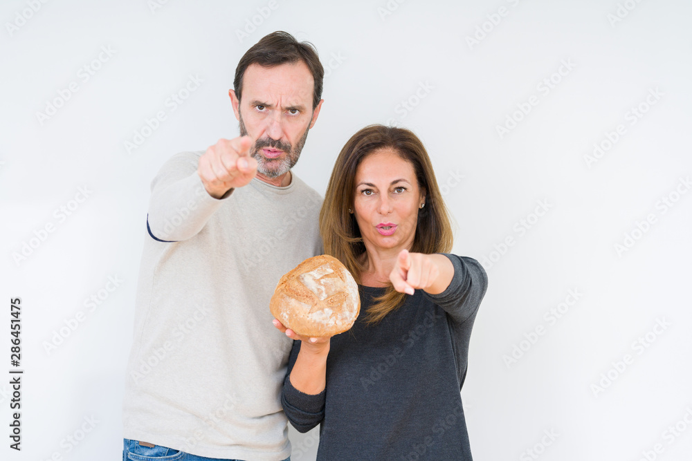 Middle age couple holding homemade fresh bread over isolated background pointing with finger to the camera and to you, hand sign, positive and confident gesture from the front Middle age couple holding homemade fresh bread over isolated background pointing with finger to the camera and to you, hand sign, positive and confident gesture from the front