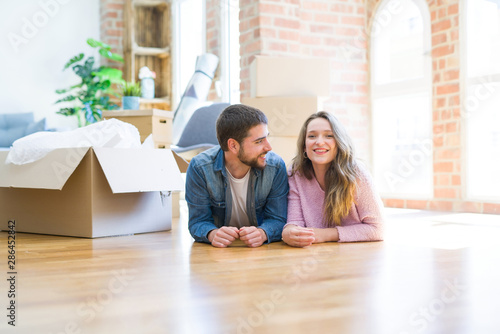 Young beautiful couple in love relaxing lying on the floor together with cardboard boxes around for moving to a new house © Krakenimages.com