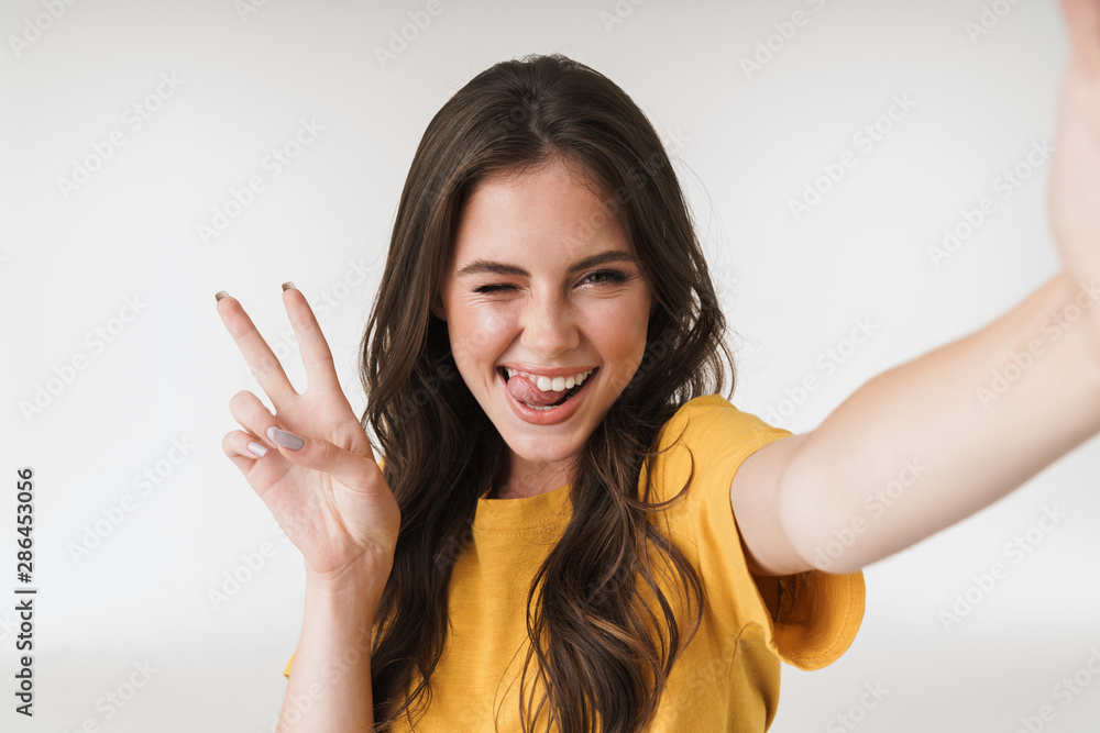 Image of amazed brunette woman smiling and showing peace sign while taking selfie photo Image of amazed brunette woman smiling and showing peace sign while taking selfie photo