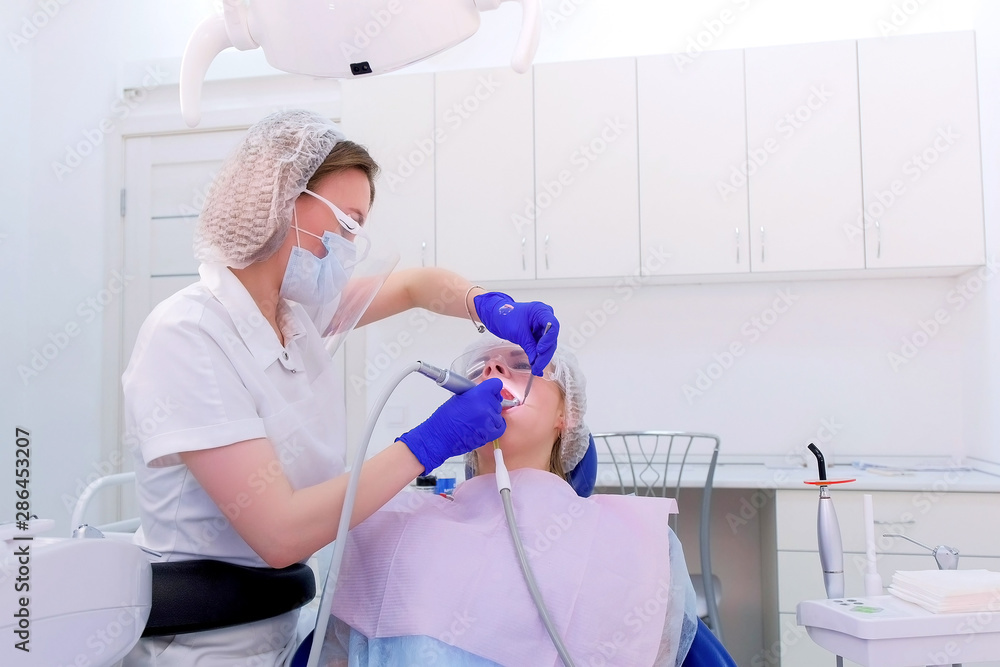 Dental hygienist cleaning and brushing woman's teeth uses drill with