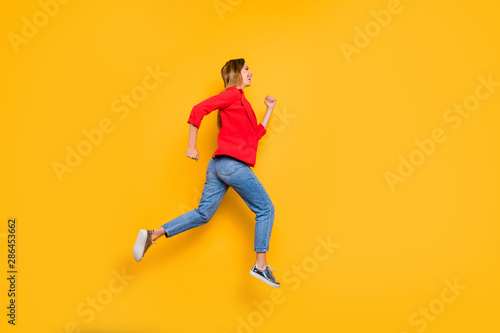 Full body profile side photo of cheerful lady running wearing red striped shirt jacket denim jeans isolated over yellow background