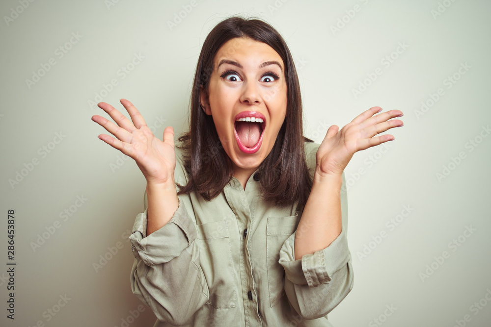 Young beautiful brunette woman wearing green shirt over isolated background celebrating crazy and amazed for success with arms raised and open eyes screaming excited. Winner concept