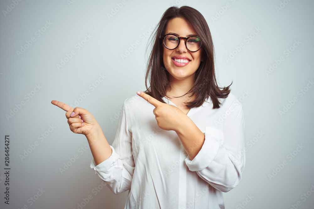Young beautiful business woman wearing glasses over isolated background smiling and looking at the camera pointing with two hands and fingers to the side. Young beautiful business woman wearing glasses over isolated background smiling and looking at the camera pointing with two hands and fingers to the side.