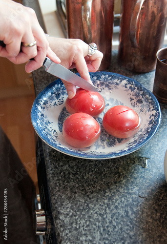 The hostess's hands use a knife to cut the tomatoes, which are covered with hot water for easy peeling.