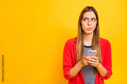 Portrait of unsure person holding gadget wearing eyewear eyeglasses isolated over yellow background