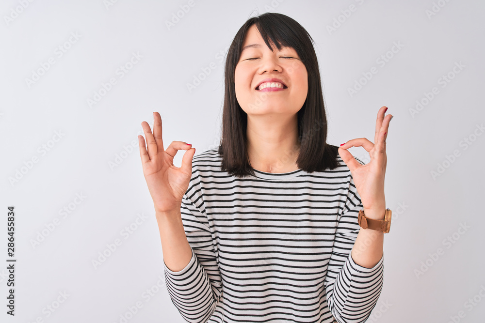 Young beautiful chinese woman wearing black striped t-shirt over isolated white background relax and smiling with eyes closed doing meditation gesture with fingers. Yoga concept. Young beautiful chinese woman wearing black striped t-shirt over isolated white background relax and smiling with eyes closed doing meditation gesture with fingers. Yoga concept.