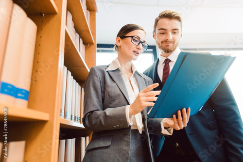 Lawyers in library of law firm discussing strategy in a case holding file photo