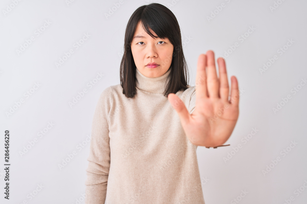 Young beautiful chinese woman wearing turtleneck sweater over isolated white background doing stop sing with palm of the hand. Warning expression with negative and serious gesture on the face. Young beautiful chinese woman wearing turtleneck sweater over isolated white background doing stop sing with palm of the hand. Warning expression with negative and serious gesture on the face.