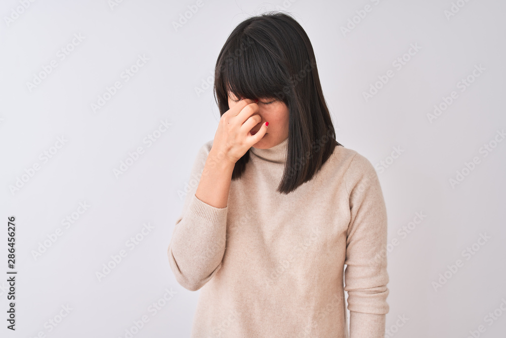 Young beautiful chinese woman wearing turtleneck sweater over isolated white background tired rubbing nose and eyes feeling fatigue and headache. Stress and frustration concept. Young beautiful chinese woman wearing turtleneck sweater over isolated white background tired rubbing nose and eyes feeling fatigue and headache. Stress and frustration concept.