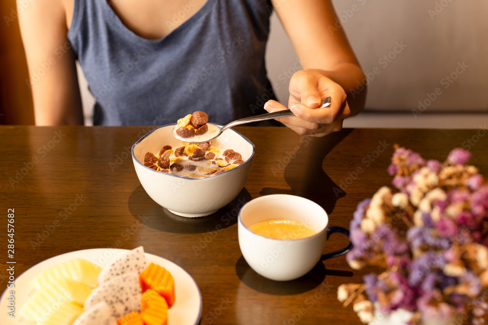 Healthy woman eating corn flakes cereal and coffee for breakfast on table.