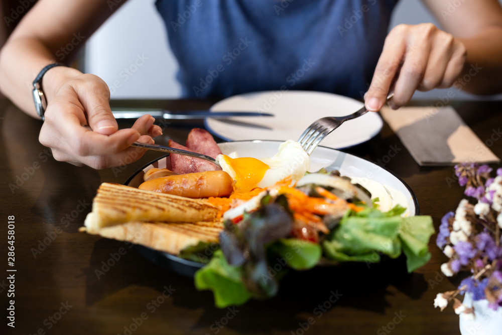 Woman having breakfast with fried eggs, sausages, vegetable salad and toast at cafe in the morning. Woman having breakfast with fried eggs, sausages, vegetable salad and toast at cafe in the morning.