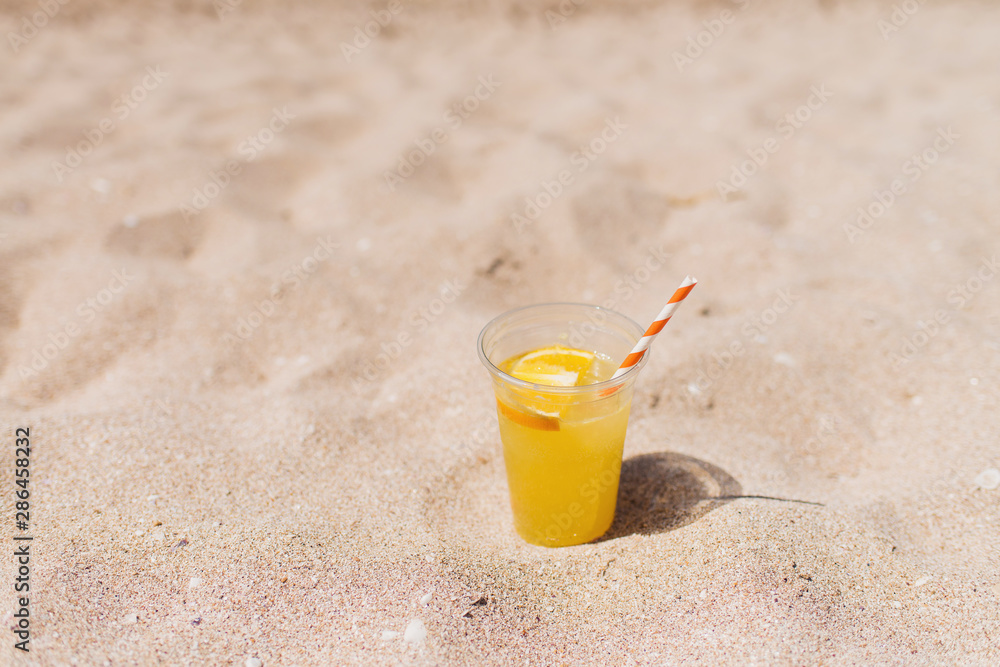 Glass of refreshing lemonade with a tube on a sand beach. Trip and summer relax concept. Copy space.