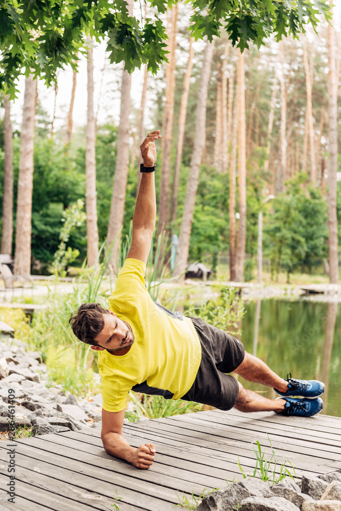 Obraz premium Athletic man in sportswear doing exercise near lake in forest