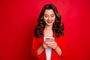 Portrait of cheerful lady with bright pomade using device wearing blazer isolated over red background