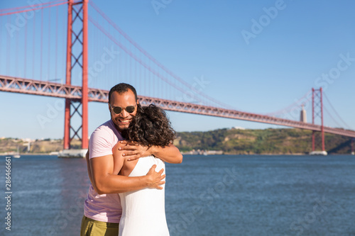 Happy couple celebrating good news and hugging. Excited man embracing his girlfriend near river with bridge in background. Couple or good news concept © Mangostar