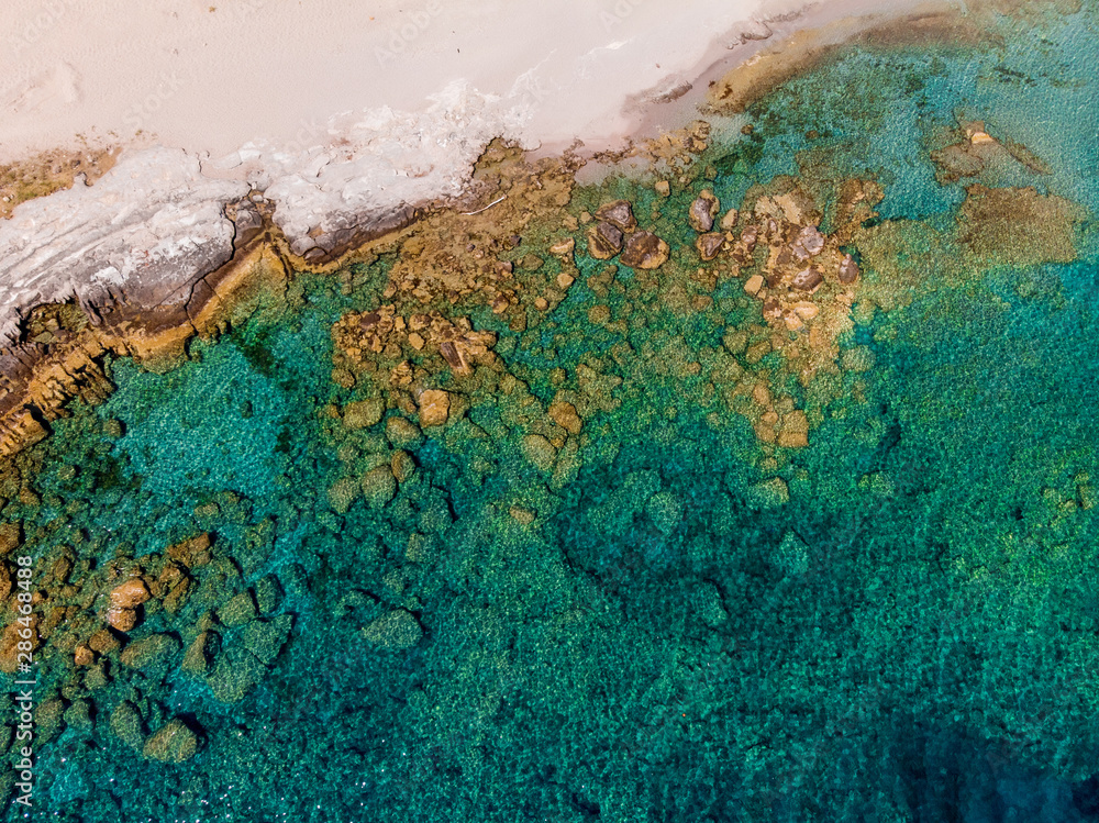 Photo of sandy shore, rusty stones, azure sea.