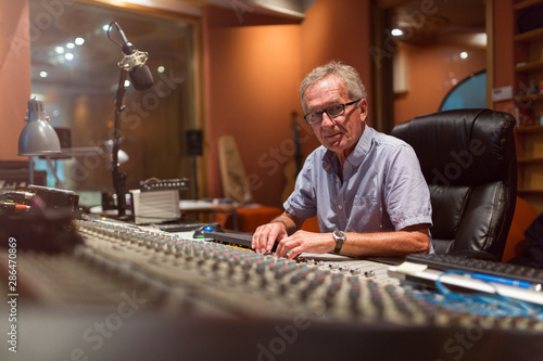 Male middle aged recording engineer in a recording studio sitting at a multi channel console photo