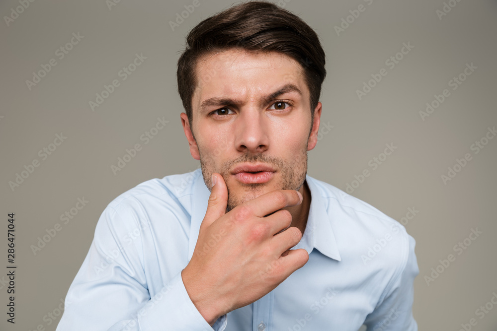 Image closeup of brooding serious man wearing formal clothes looking at camera and touching his chin Image closeup of brooding serious man wearing formal clothes looking at camera and touching his chin