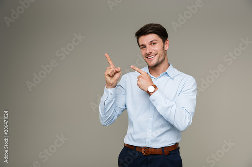 Image of cheerful brunette man wearing formal clothes smiling and pointing finger aside at copyspace