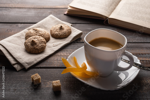 Cup of black coffee with candied oranges and lumps of sugar. Ccookies on a linen napkin and an open book