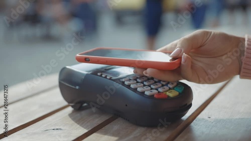 Customer paying for order in the cafe with payment terminal using NFC smartphone technology girl applying mobile phone on cash machine device digital e-money e-wallet electronic close up slow motion