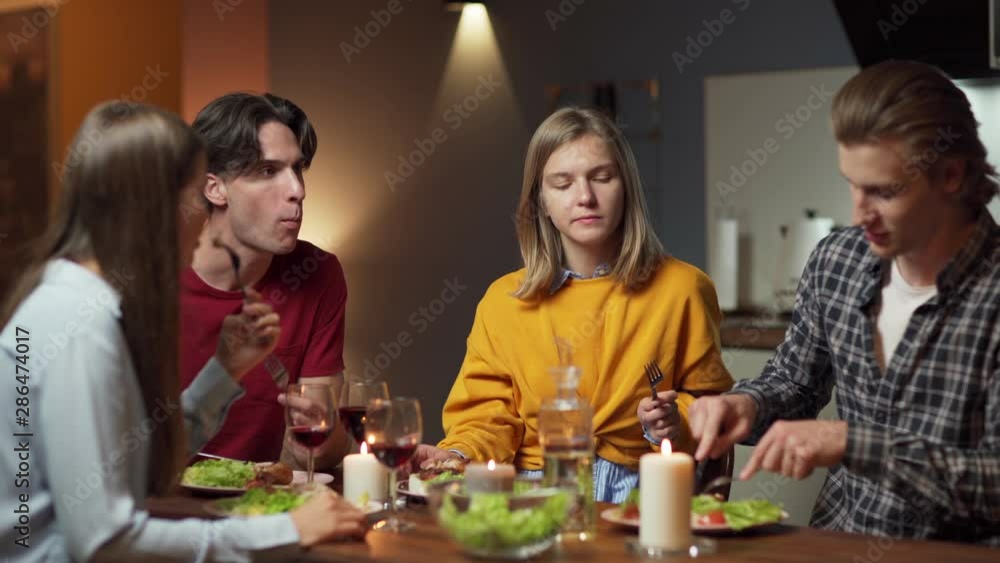 Zoom out shot of four friends, two couples, dining together at home. Young people enjoying delicious meal and talking over dinner and wine Zoom out shot of four friends, two couples, dining together at home. Young people enjoying delicious meal and talking over dinner and wine