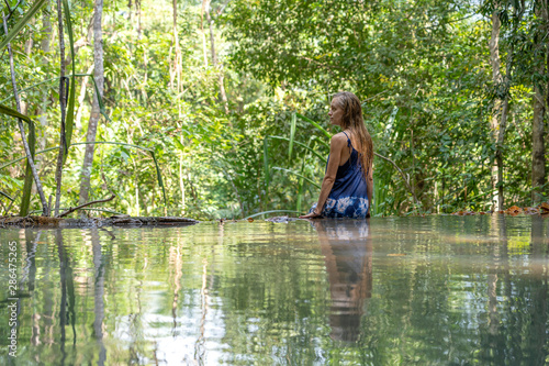 Young woman near turquoise water of cascade waterfall at tropical rain forest, island Koh Phangan, Thailand