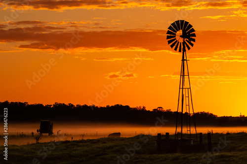 Silhouette of windmill on farmland against orange yellow sky