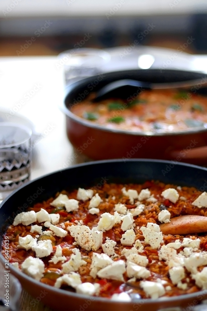 Two pots of orzo pasta, with tomato sauceand vegetables. One with seafood, one vegetarian with feta cheese, served on a table. Selective focus. Two pots of orzo pasta, with tomato sauceand vegetables. One with seafood, one vegetarian with feta cheese, served on a table. Selective focus.