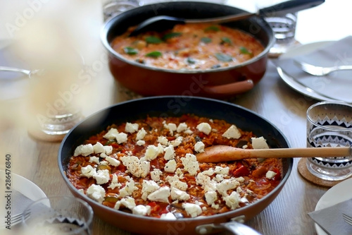 Two pots of orzo pasta, with tomato sauceand vegetables. One with seafood, one vegetarian with feta cheese, served on a table. Selective focus.