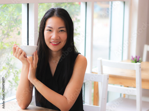Free Download Asian woman holding cup of coffee smiling and looking to the camera. - GFXLoad