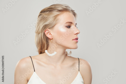 Pretty woman with blonde hair, makeup and fashion golden earrings with nacre on white background. Perfect profile