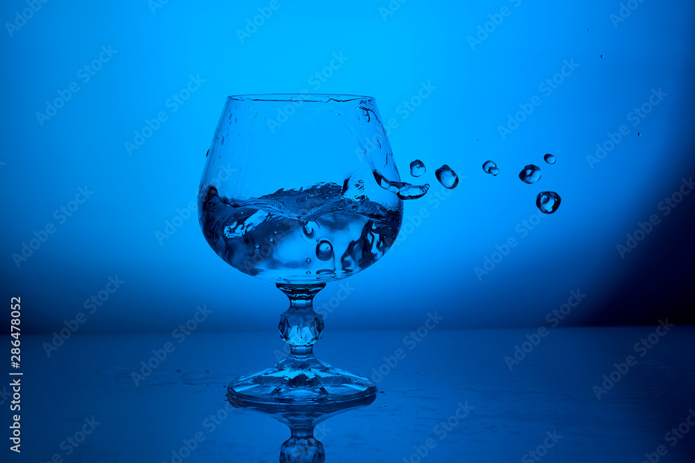 Clear water splash in glass with drops on blue lighting background Clear water splash in glass with drops on blue lighting background