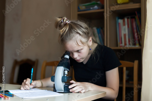 Girl 12 years old doing homework in chemistry with microscope.