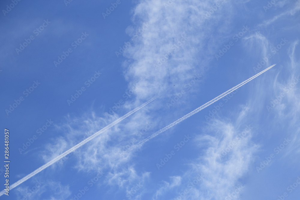 Airplanes leaves trace on among cloud on blue sky. View from below on the trails from plane. Travel concept background.