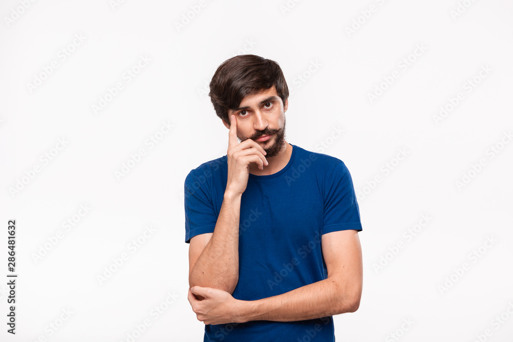 Thoughtful handsome brunet man in a blue shirt holding arms folded over his chest and keeping one hand close to face standing isolated over white background. Thoughtful handsome brunet man in a blue shirt holding arms folded over his chest and keeping one hand close to face standing isolated over white background.