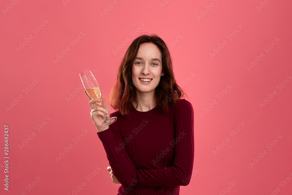 Excited pretty brunette girl holding wineglass of sparkling champagne standing isolated on a dark pink background and smiling at the camera. Excited pretty brunette girl holding wineglass of sparkling champagne standing isolated on a dark pink background and smiling at the camera.
