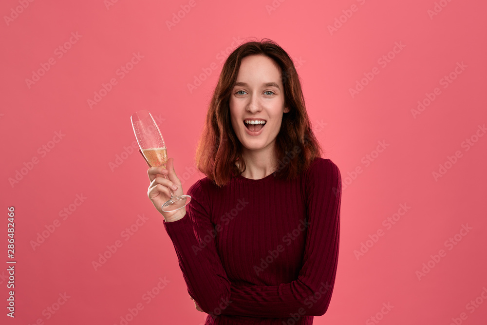 Excited pretty brunette girl holding wineglass of sparkling champagne standing isolated on a dark pink background and smiling at the camera. Excited pretty brunette girl holding wineglass of sparkling champagne standing isolated on a dark pink background and smiling at the camera.
