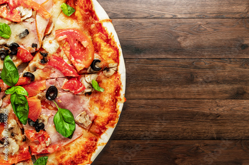 Pizza on a wooden background with ham, olives, tomatoes and green basil. Itolyan cuisine, copy space.